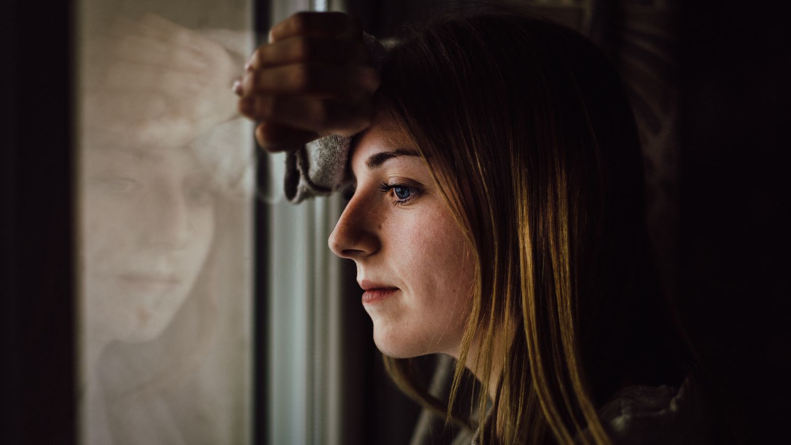 Young woman sitting by a window, thinking about living with alopecia areata