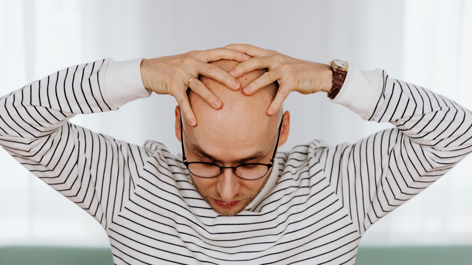 Man holding his head, considering the androgenic alopecia triggers behind a receding hairline