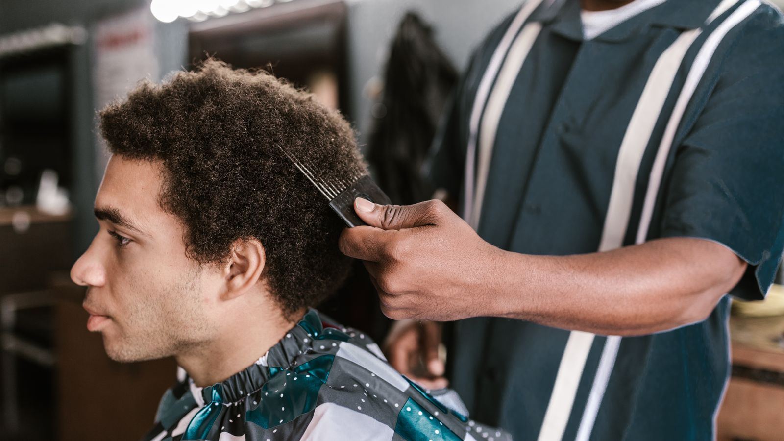 Barber styling a black man's afro hair with an afro pick