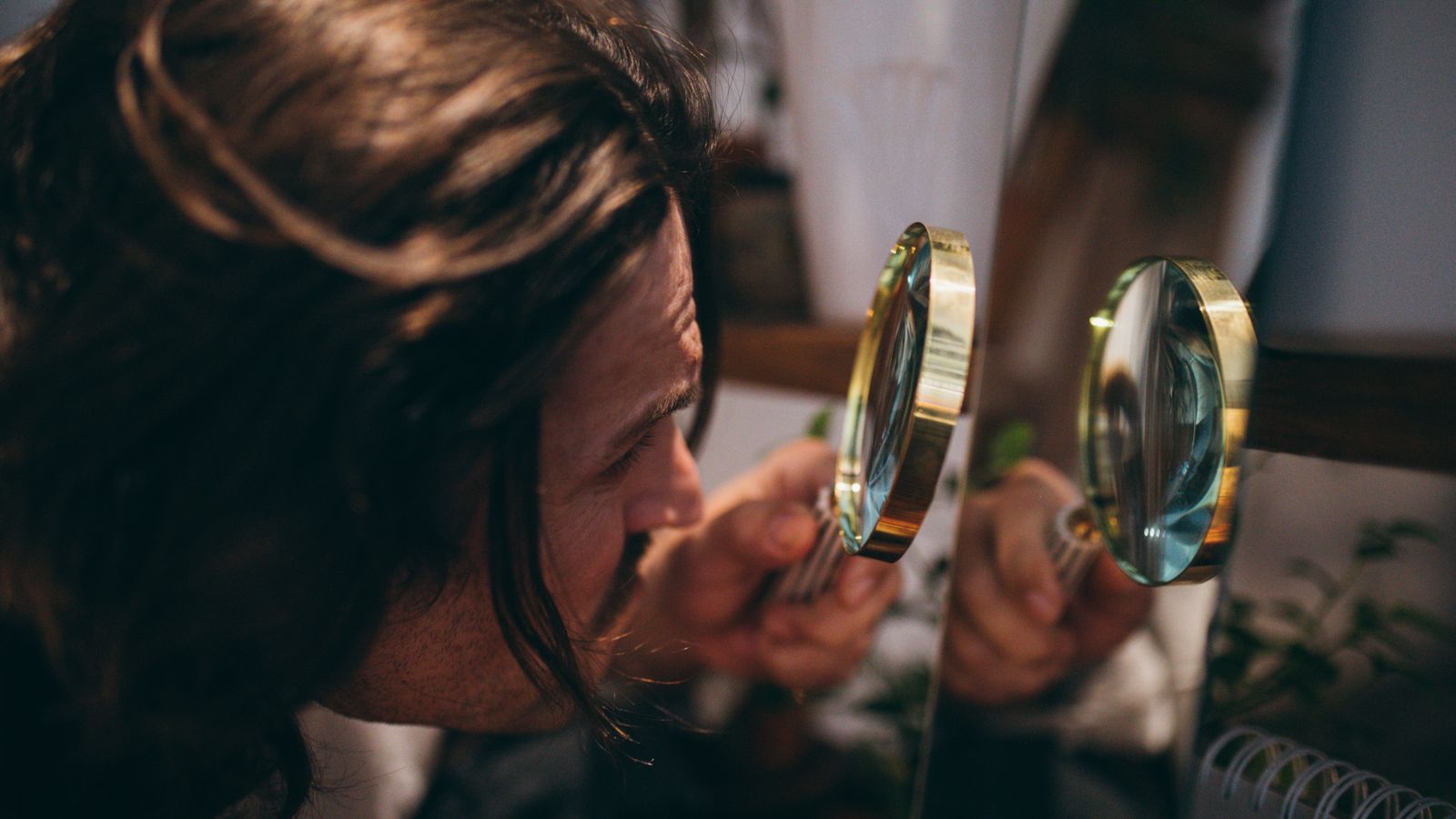 Close-up of a man using a magnifying glass to inspect his hair, illustrating how DHT and hair loss are assessed strand by strand