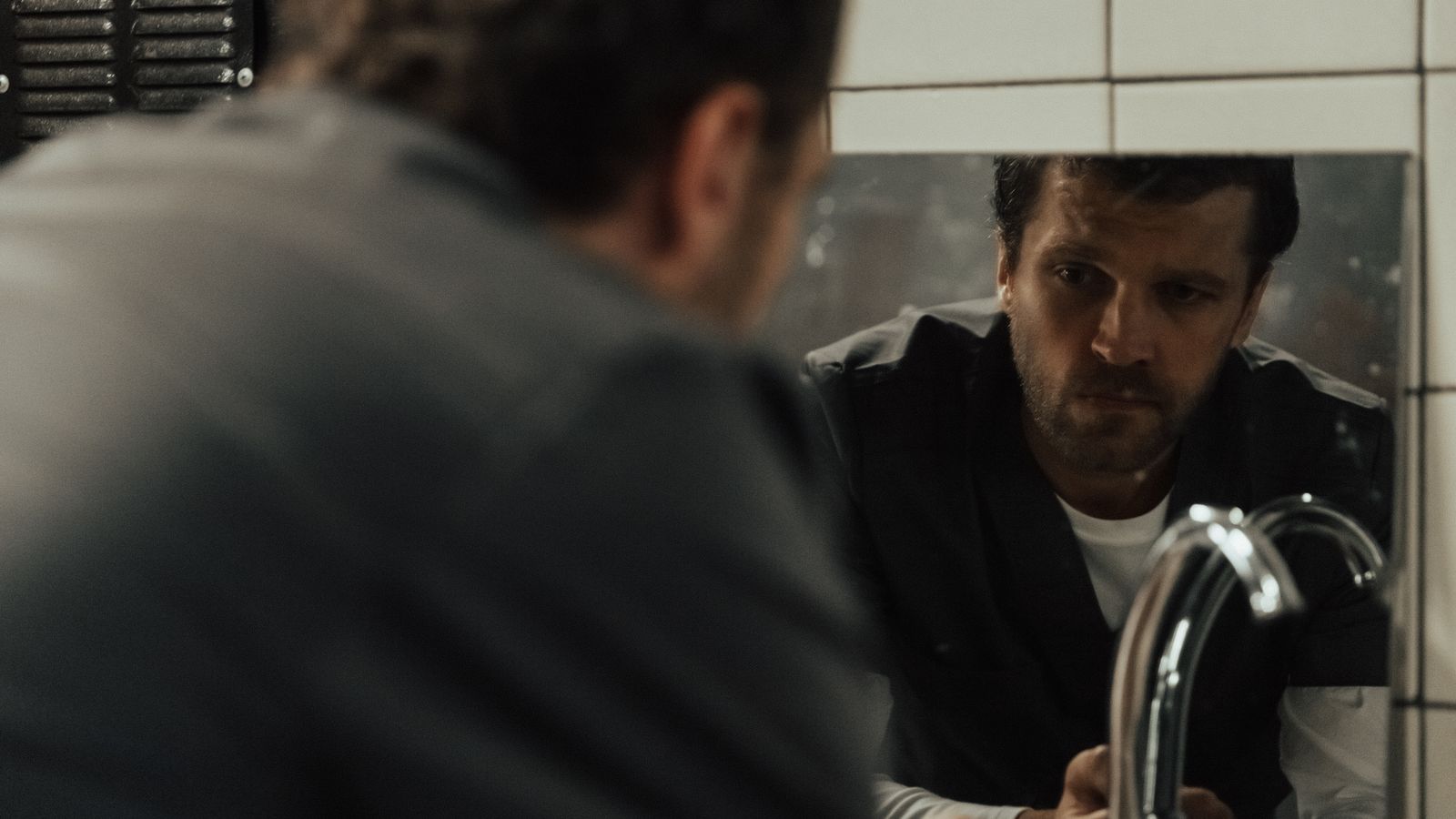 A man looking thoughtfully into a bathroom mirror while weighing his DHT hair loss options