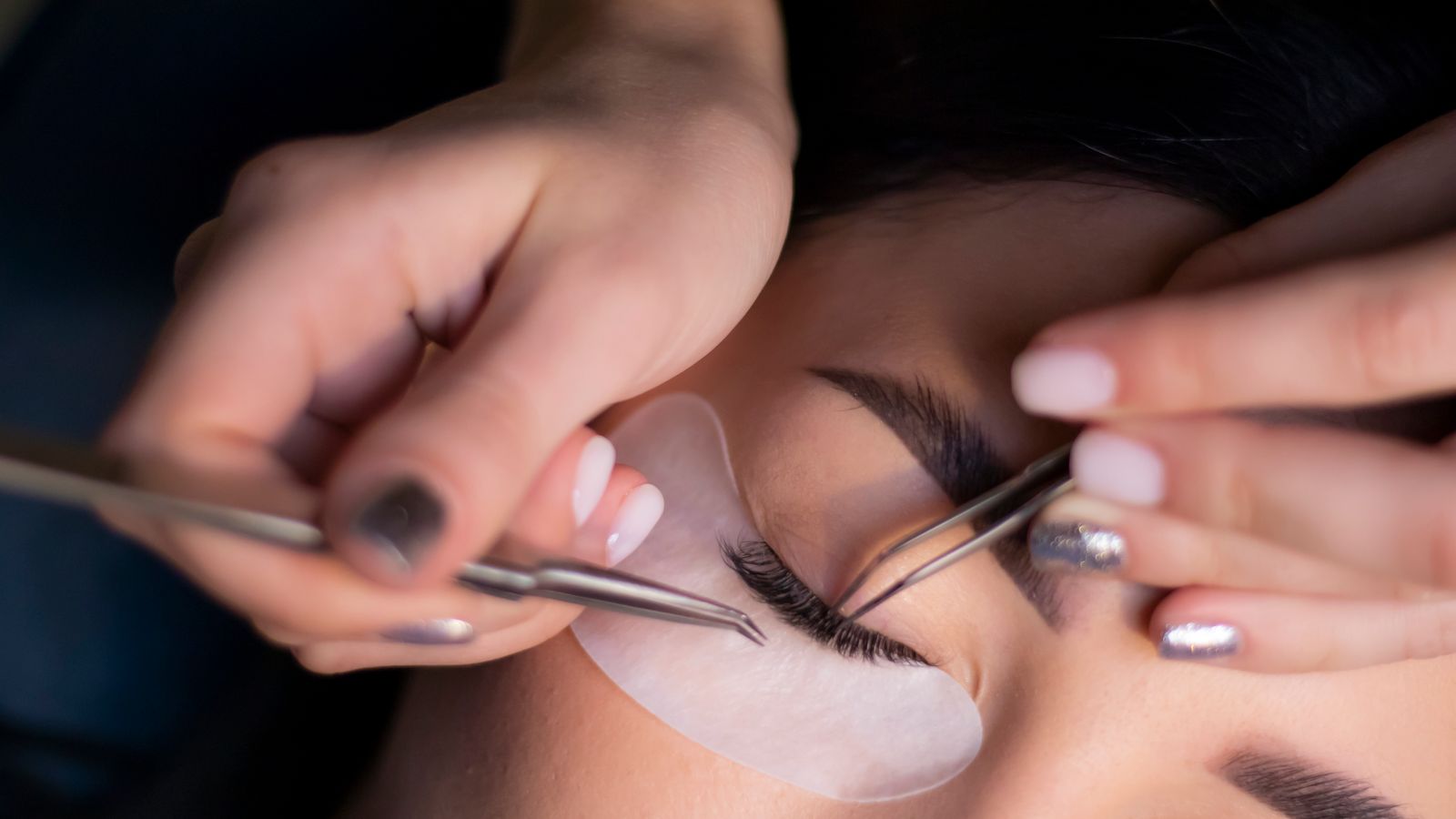Beautician applying eyelash extensions with tweezers, the salon service most likely to damage natural lashes