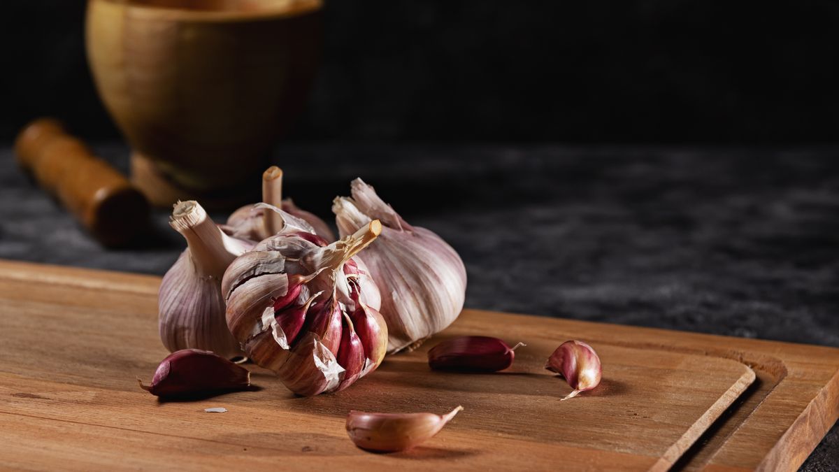 Garlic bulbs and cloves on a wooden board with a mortar, the home remedy behind the question does garlic kill candida