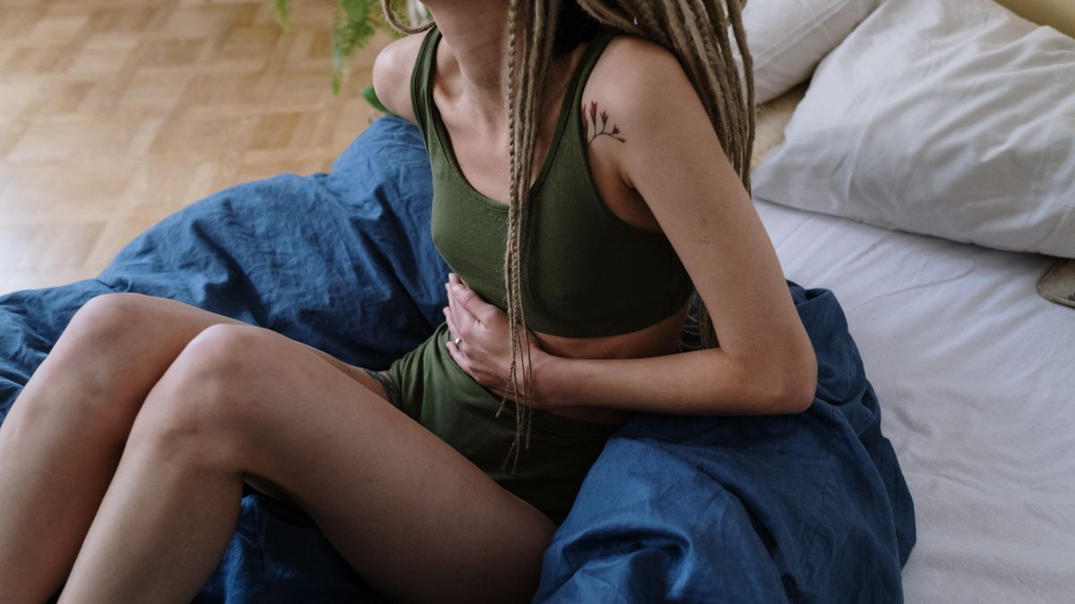 Woman sitting in bed holding her upper abdomen, the classic location of gallstones symptoms and biliary pain