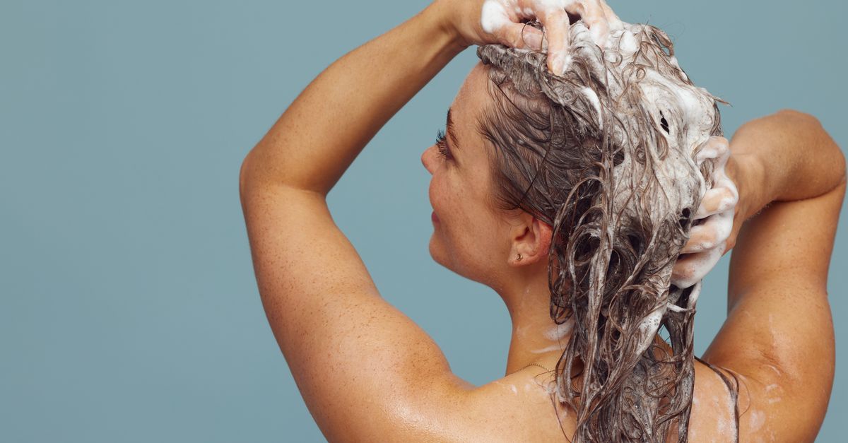 A woman lathering shampoo through long hair, the single biggest lever on greasy hair