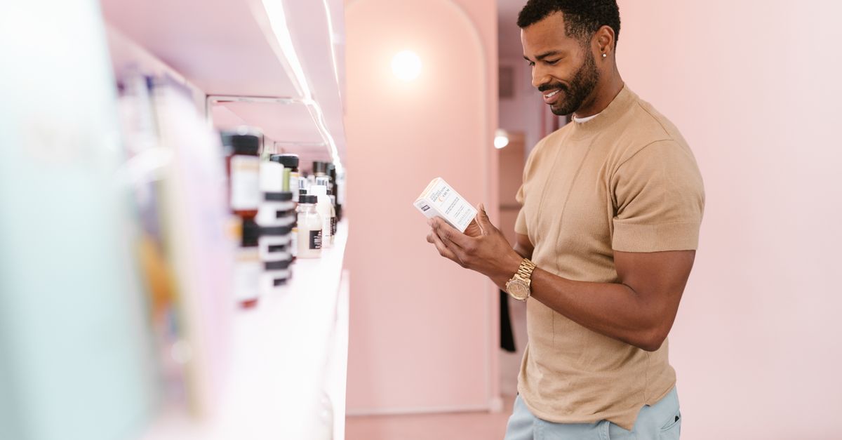 A man reading a product label in a shop, comparing options for hair care without medication