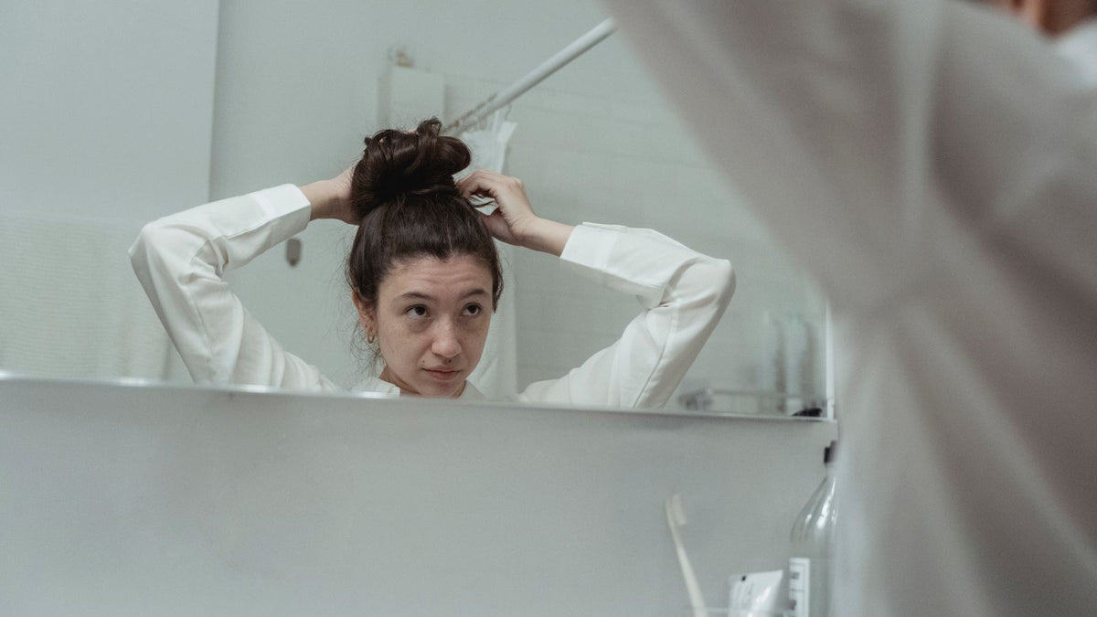 Woman styling her hair at a bathroom mirror, hair growth peptides for women side effects