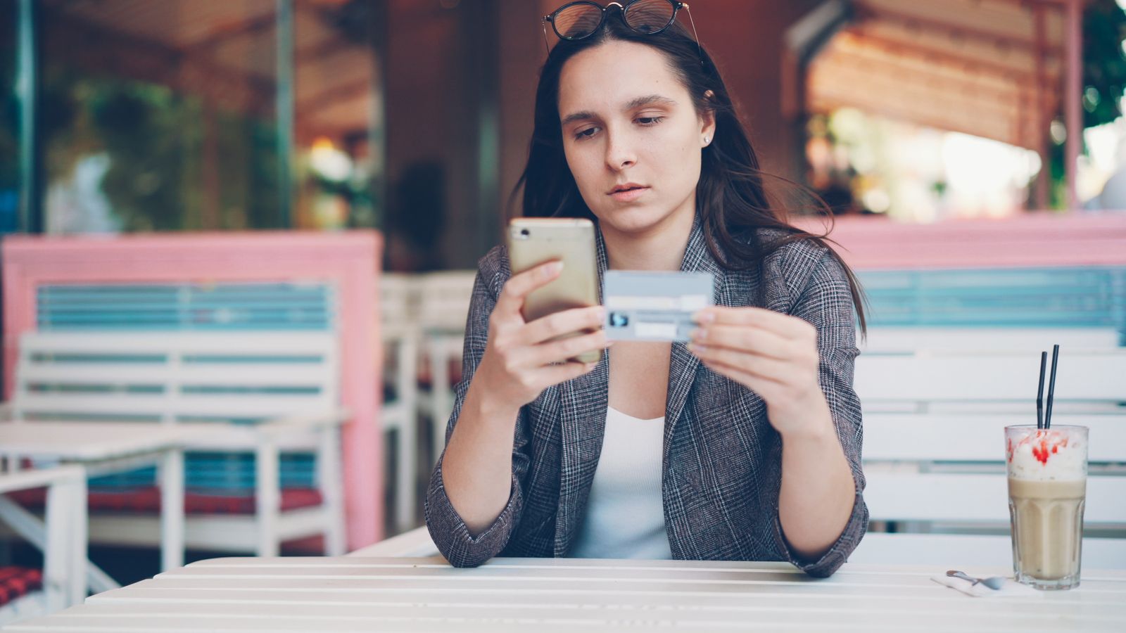 Woman reading hair growth product reviews on her phone in a cafe before buying