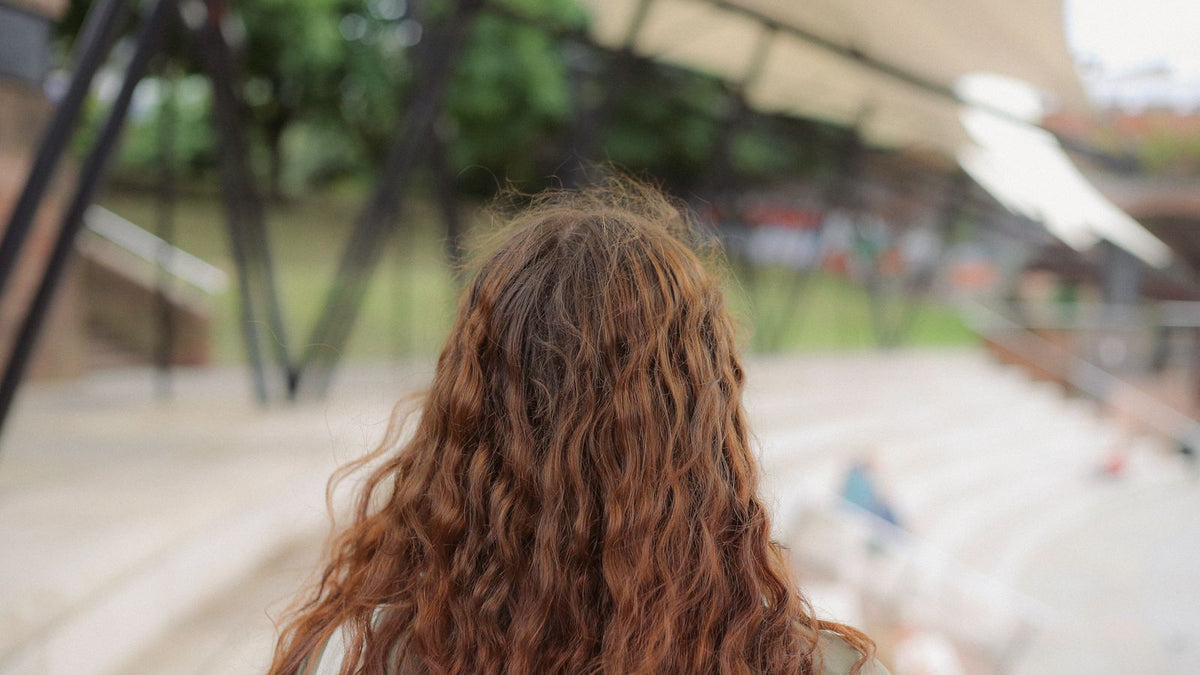 Back view of long wavy red hair with frizz at the crown, a common sign of hair porosity at work