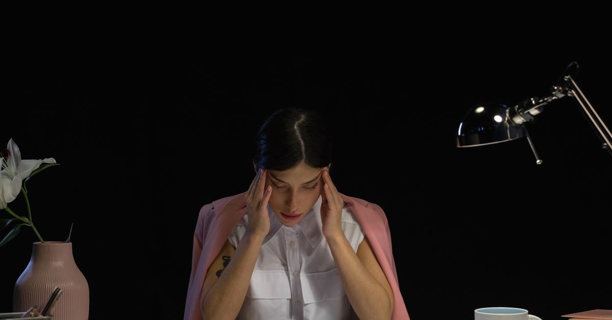 A woman sitting at a desk with her head in her hands, the stressful period that comes before hair recovery after stress