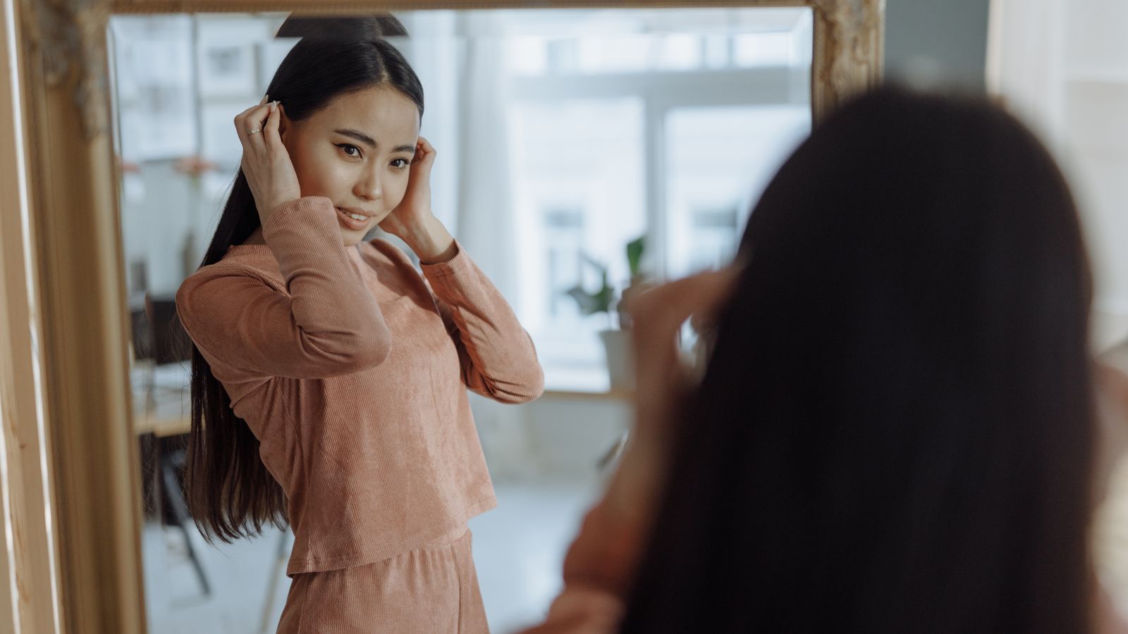 Woman adjusting her hair in front of a mirror, checking for hair recovery after weight loss