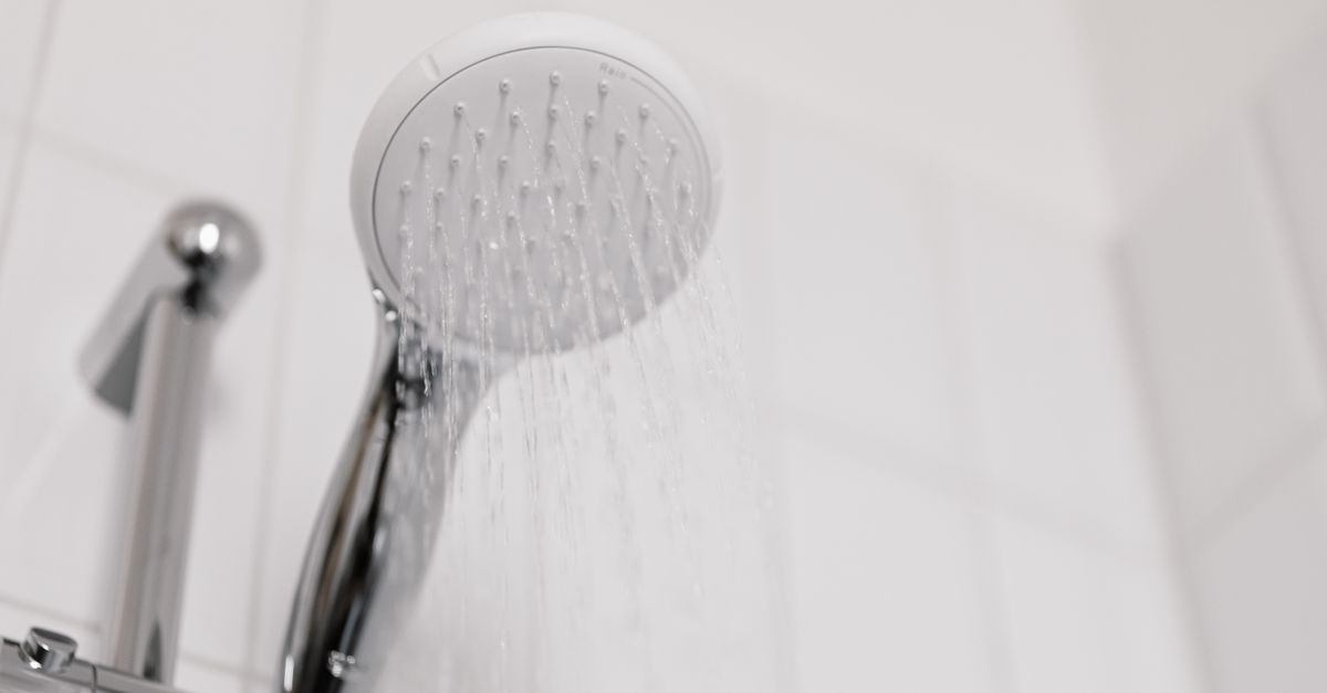 A shower head running in a tiled bathroom, the daily contact point between hard water and hair