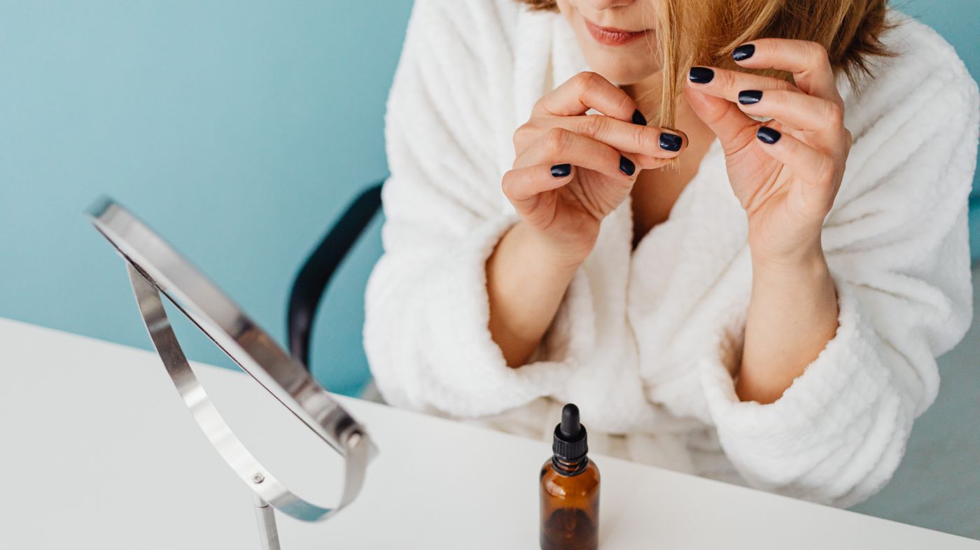 Woman applying hair oil at the mirror, one of the most common home remedies for hair