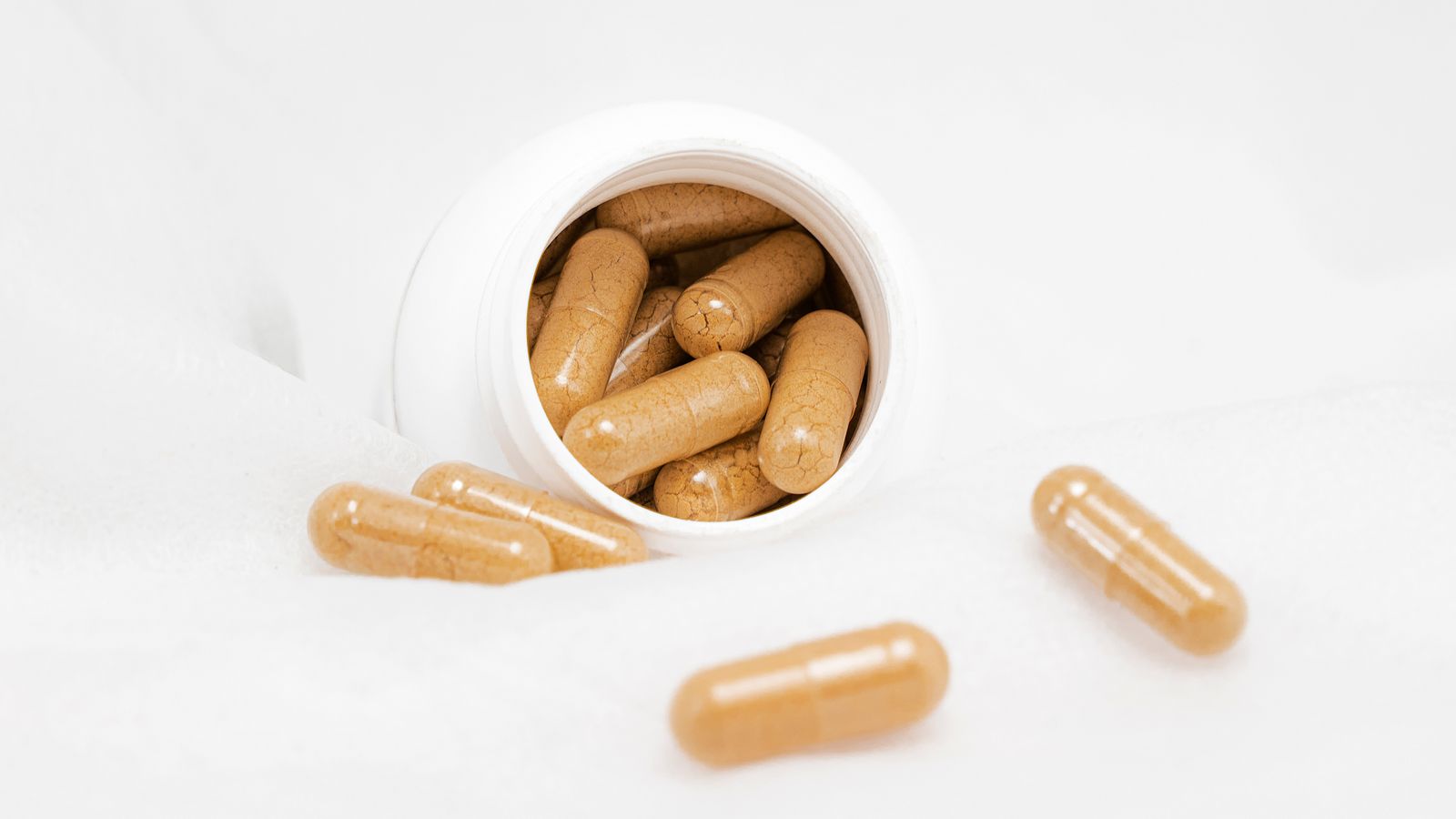 Capsules spilling from a white bottle, the supplements people reach for when researching hormone therapy hair vitamins