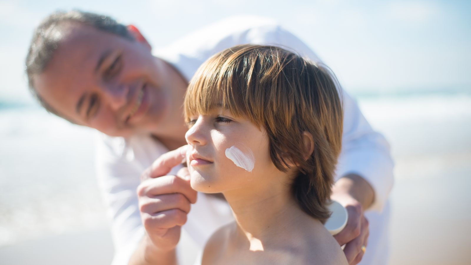 A parent applying sunscreen to a child's face on a sunny day, showing how much sunscreen to use on the face