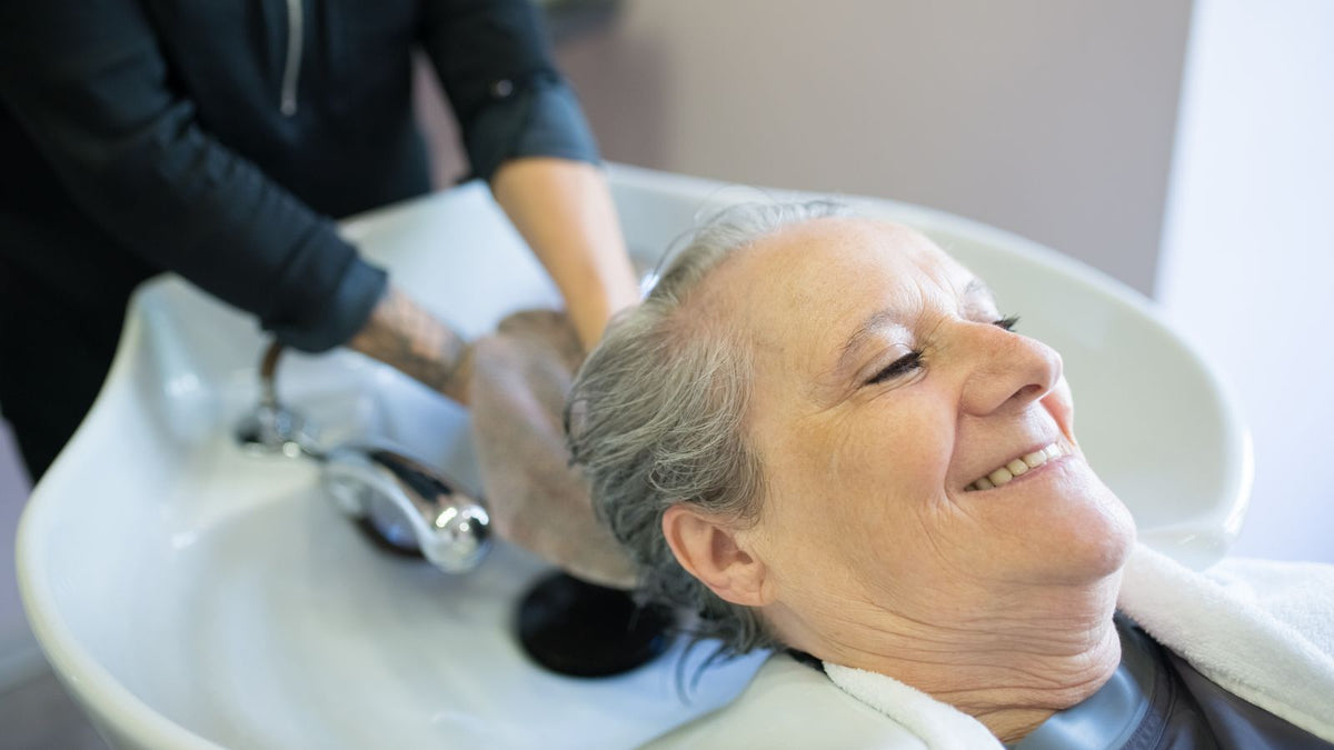 Smiling woman having her hair washed at a salon sink, wondering how often should you wash your hair