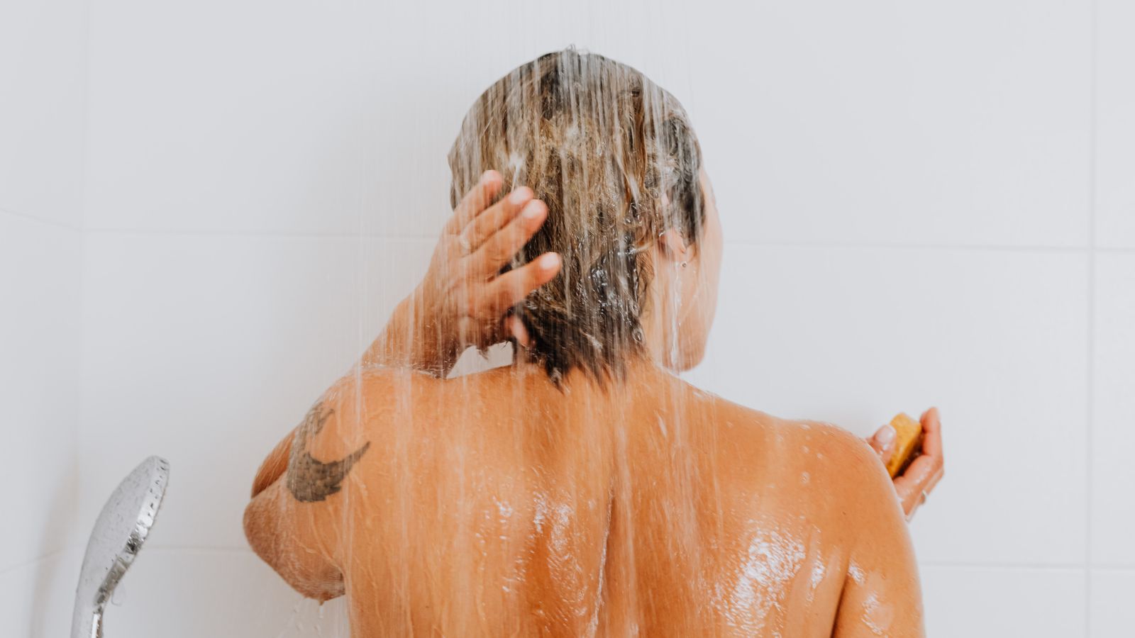 Woman rinsing her hair under the shower, deciding how often to wash her hair