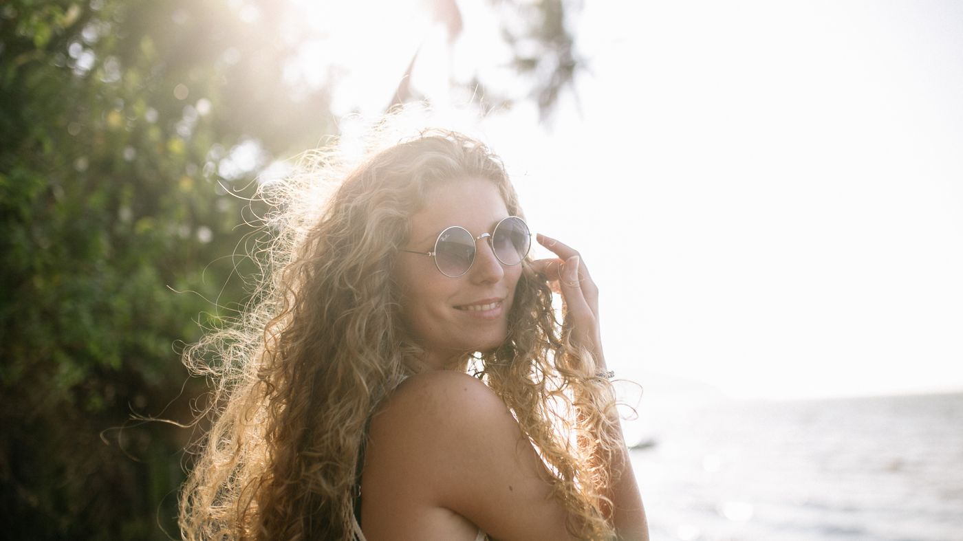 Woman with curly hair by the sea in bright sunshine, illustrating how to protect hair from the sun