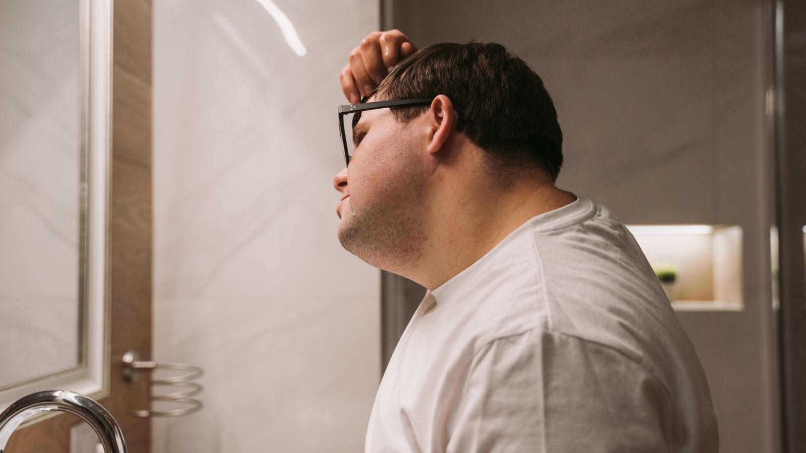 Man looking in a bathroom mirror working out how to tell if hairline is receding