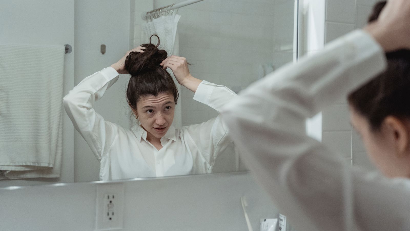Woman studying her hair in a bathroom mirror, working out how to tell if your hair is thinning