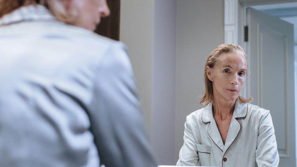 Woman looking in the bathroom mirror at her hair after HRT discontinuation