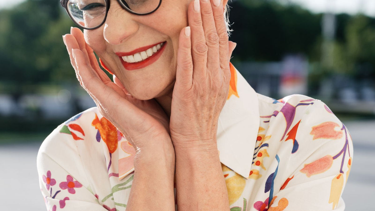 Smiling senior woman with glasses outdoors, thinking about HRT duration and her hair over the years