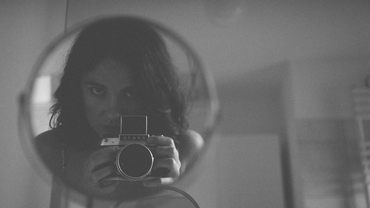 Black and white self portrait in a round mirror, the kind of photo that makes HRT hair monitoring easy