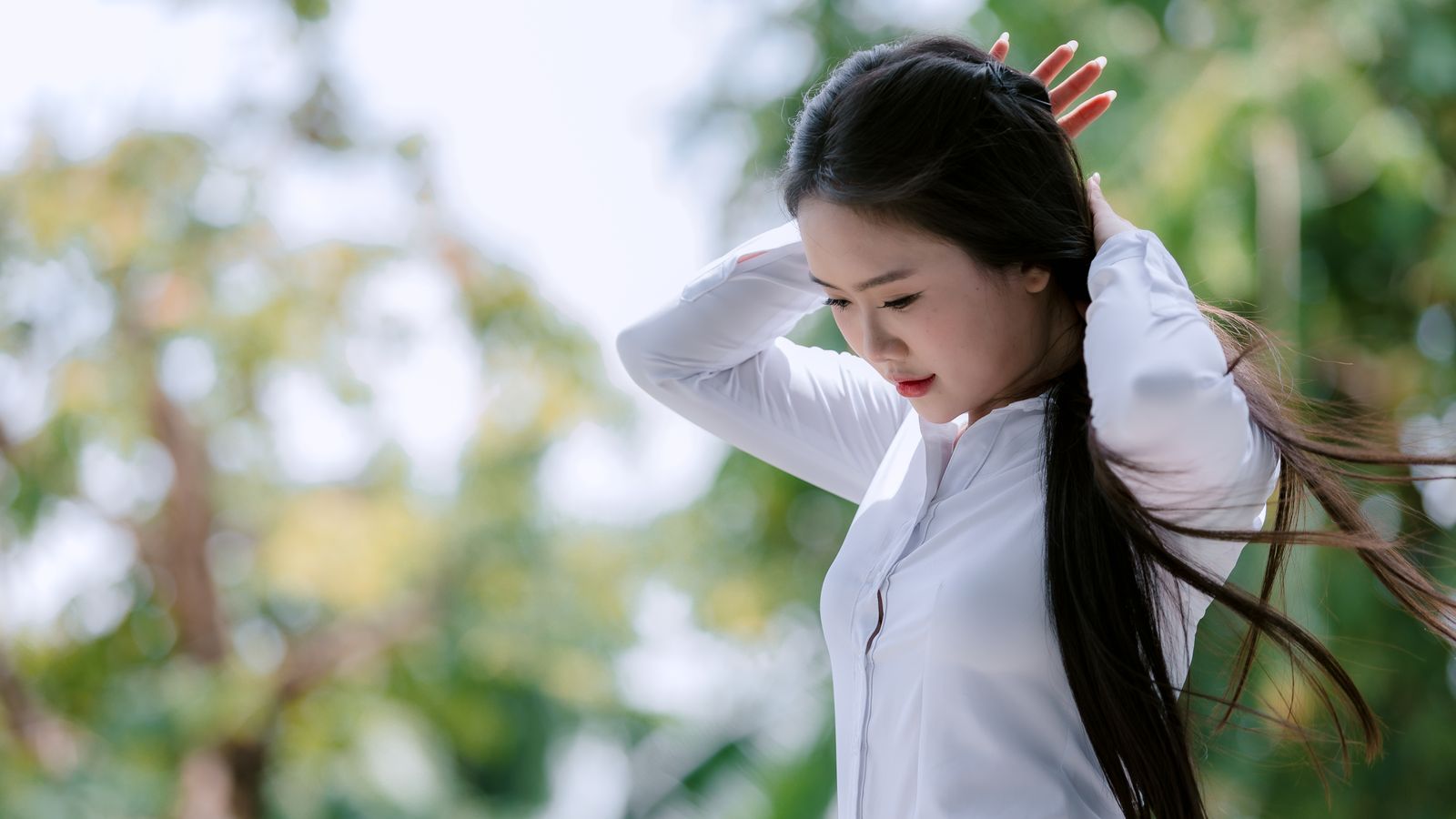 Woman in a white shirt adjusting her hair outdoors, HRT hair strength and reducing breakage