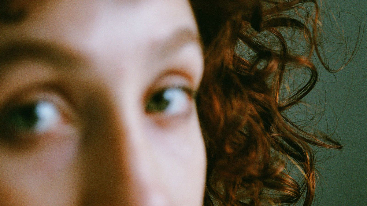Blurred close-up of a woman's face featuring curly hair and eyes, with a focus on artistic expression, illustrating HRT hair texture