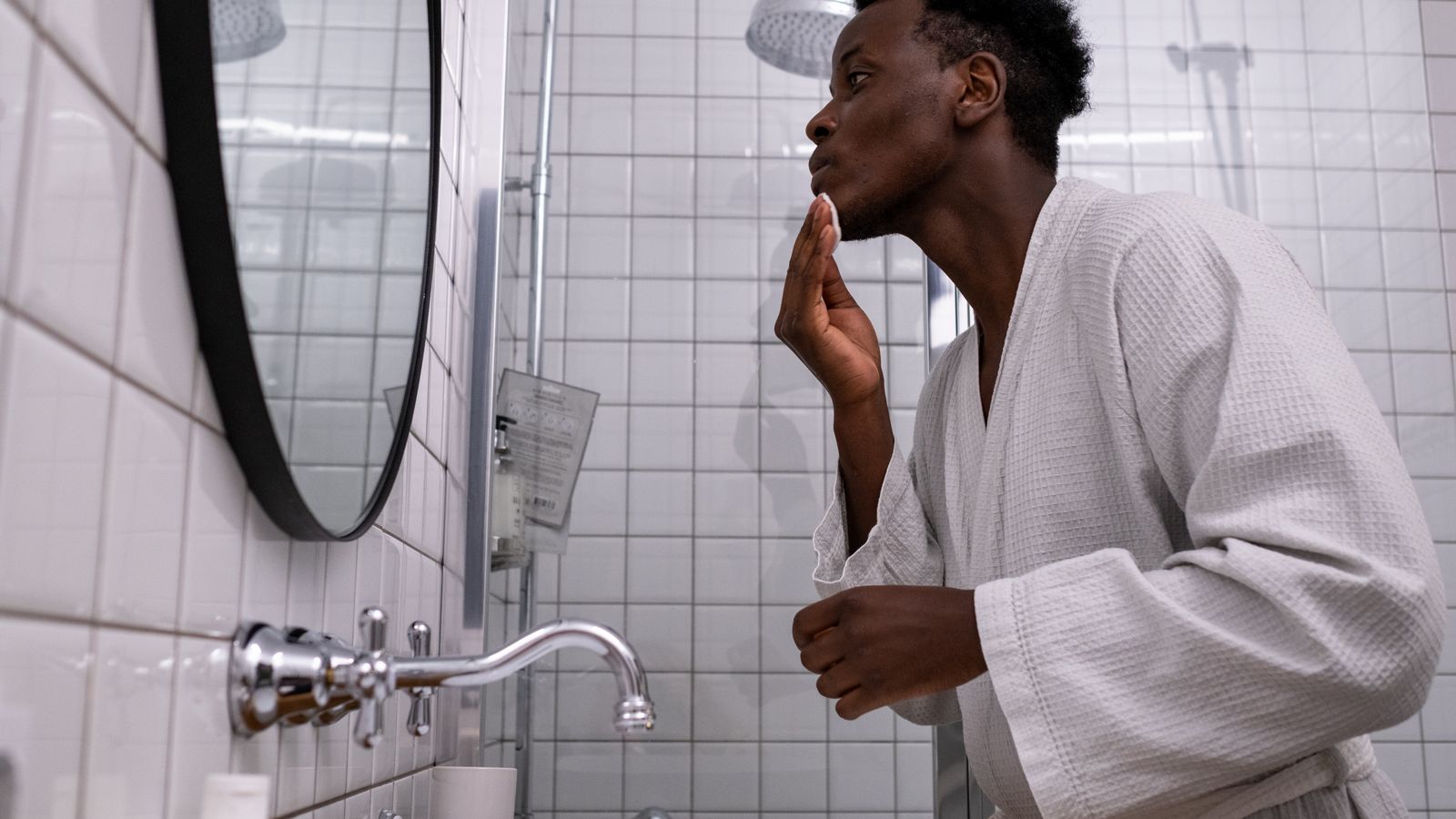 Man at a bathroom mirror working through a morning routine, HRT scalp care starts with washing frequency