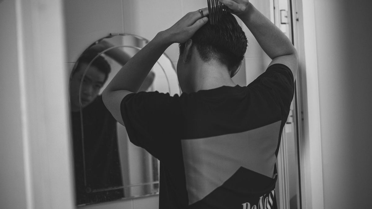 Man combing his hair in the mirror after noticing a McDonalds hairline