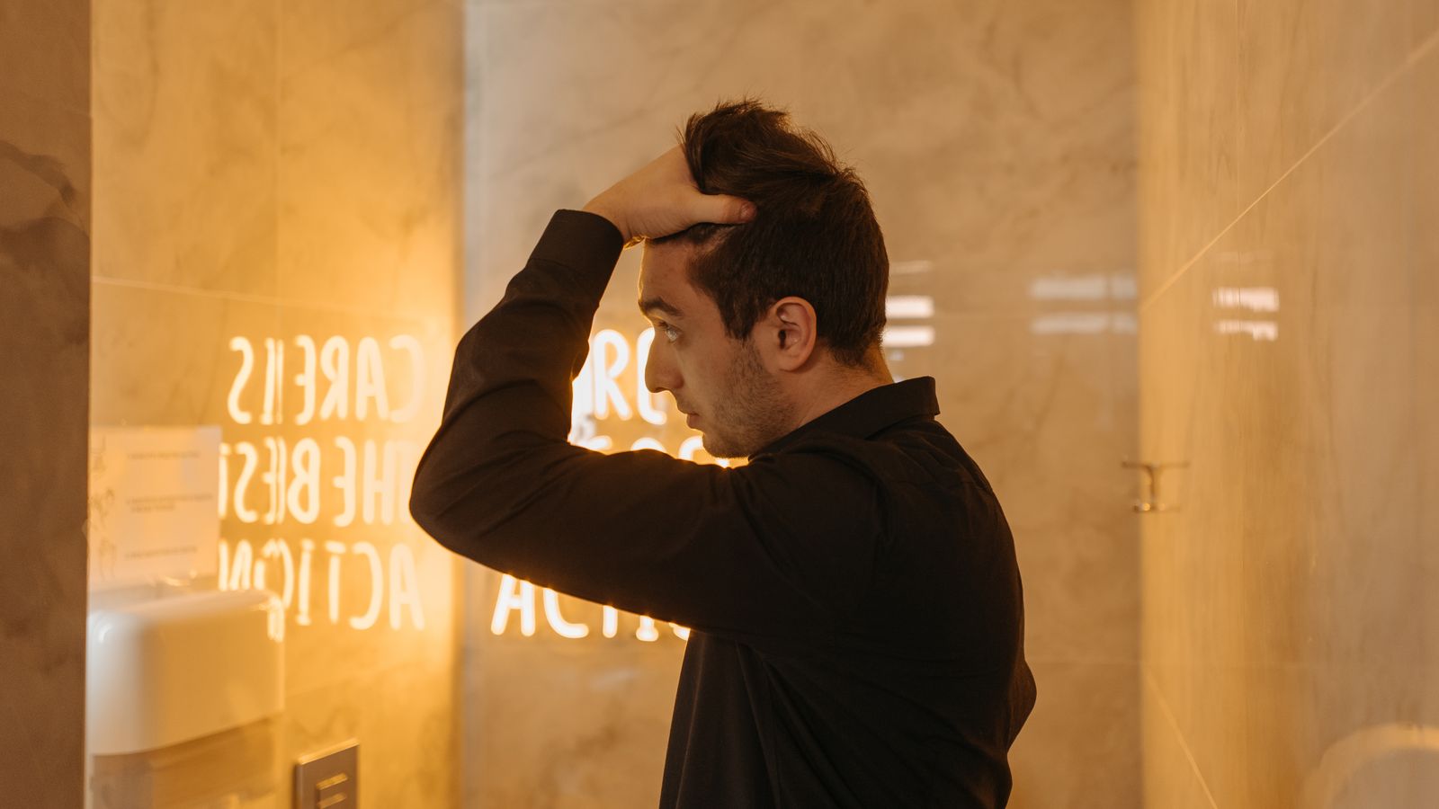 Man in a bathroom mirror weighing up the non-surgical hair restoration men in the UK can choose from