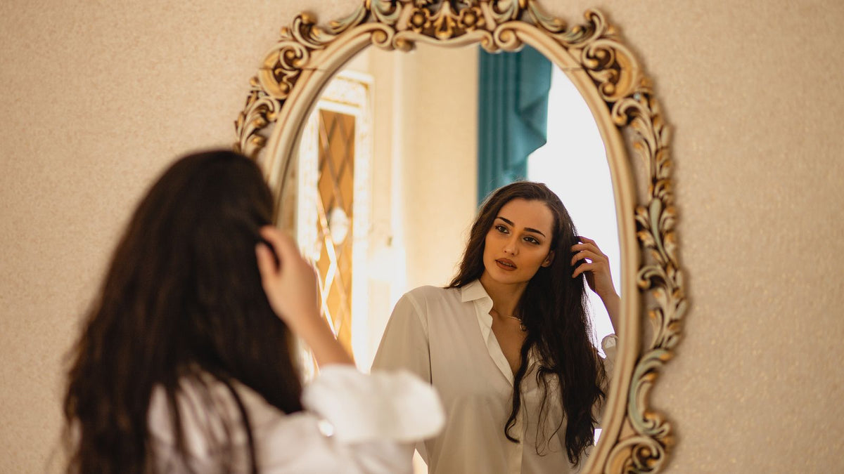 Woman with long brunette hair looking at her reflection before starting pre HRT haircare