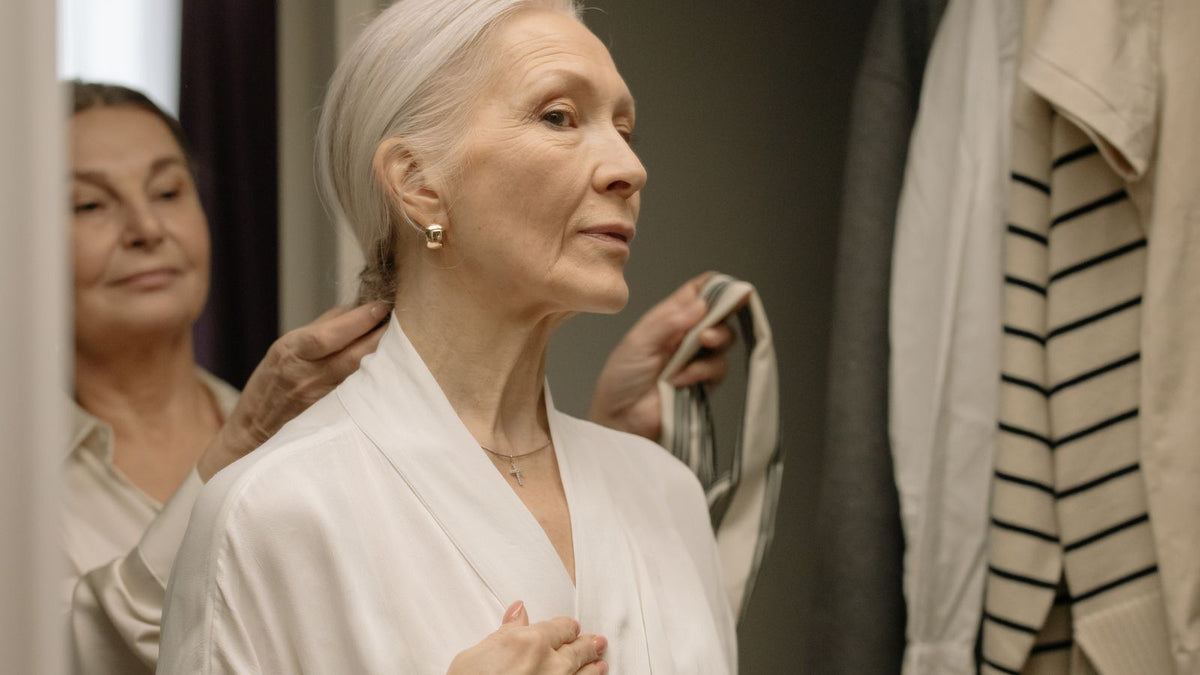 Choosing a shampoo for older hair: a senior woman in a white robe smoothing her hair at home