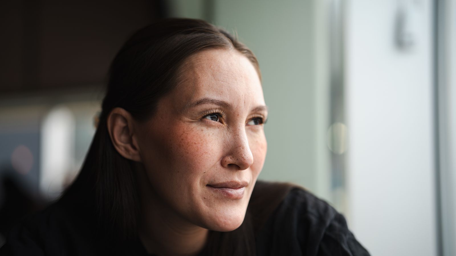 Woman gazing out of a window in soft natural light, reflecting on stress hair shedding