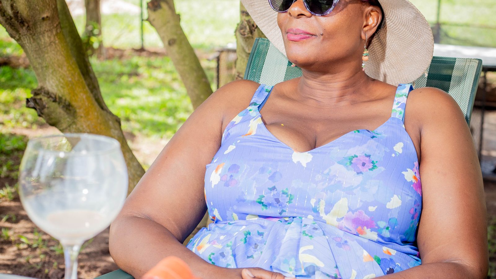 Woman in a sun hat and sunglasses sitting in the shade, using a full sun protection guide