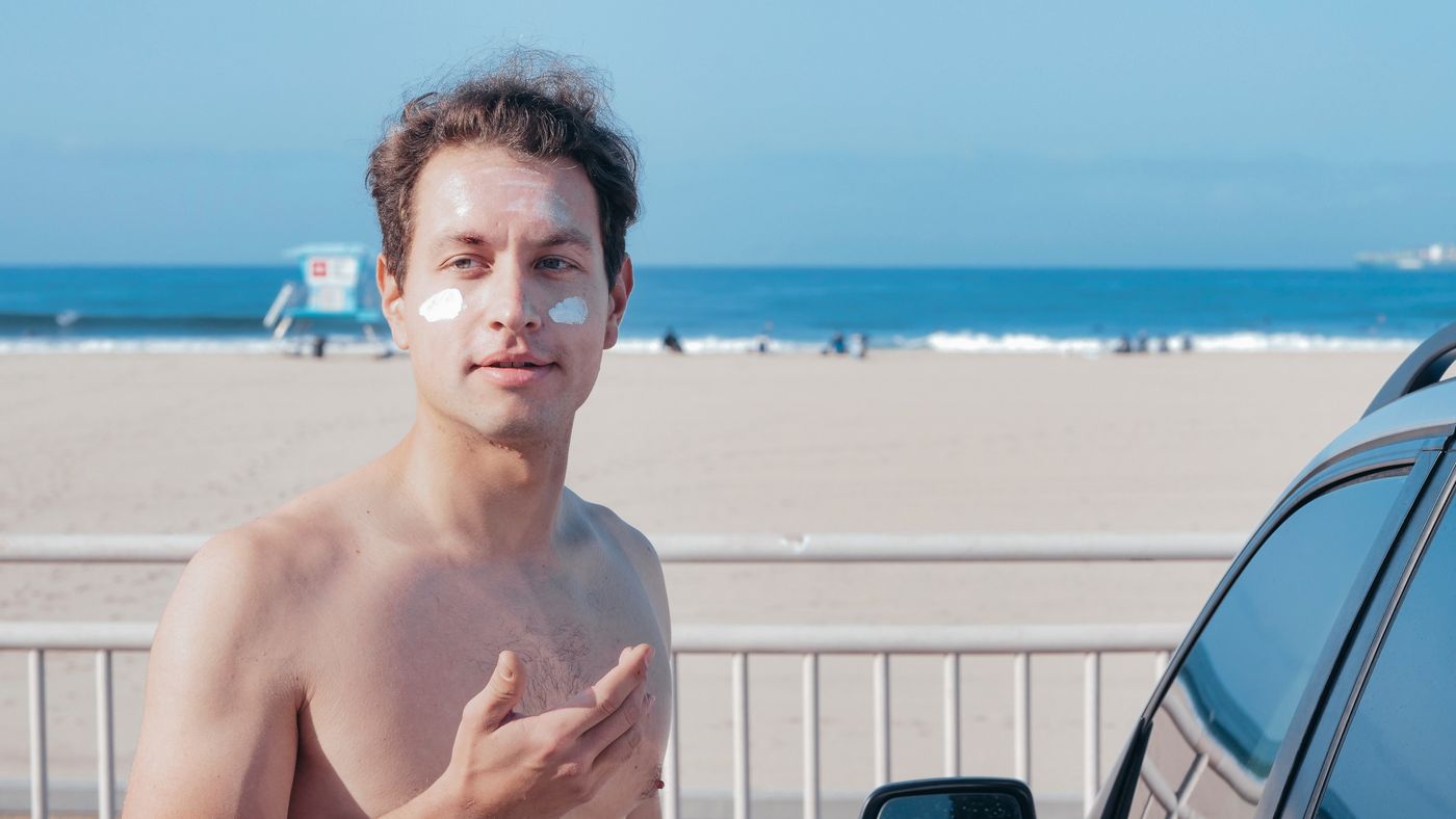 Man applying sunscreen for men to his face on a sunny beach day