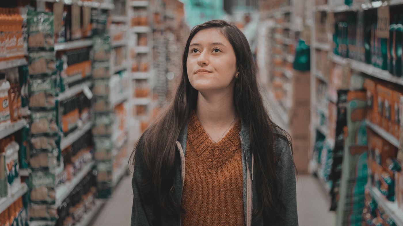 Woman browsing a supermarket aisle while choosing supermarket skincare products