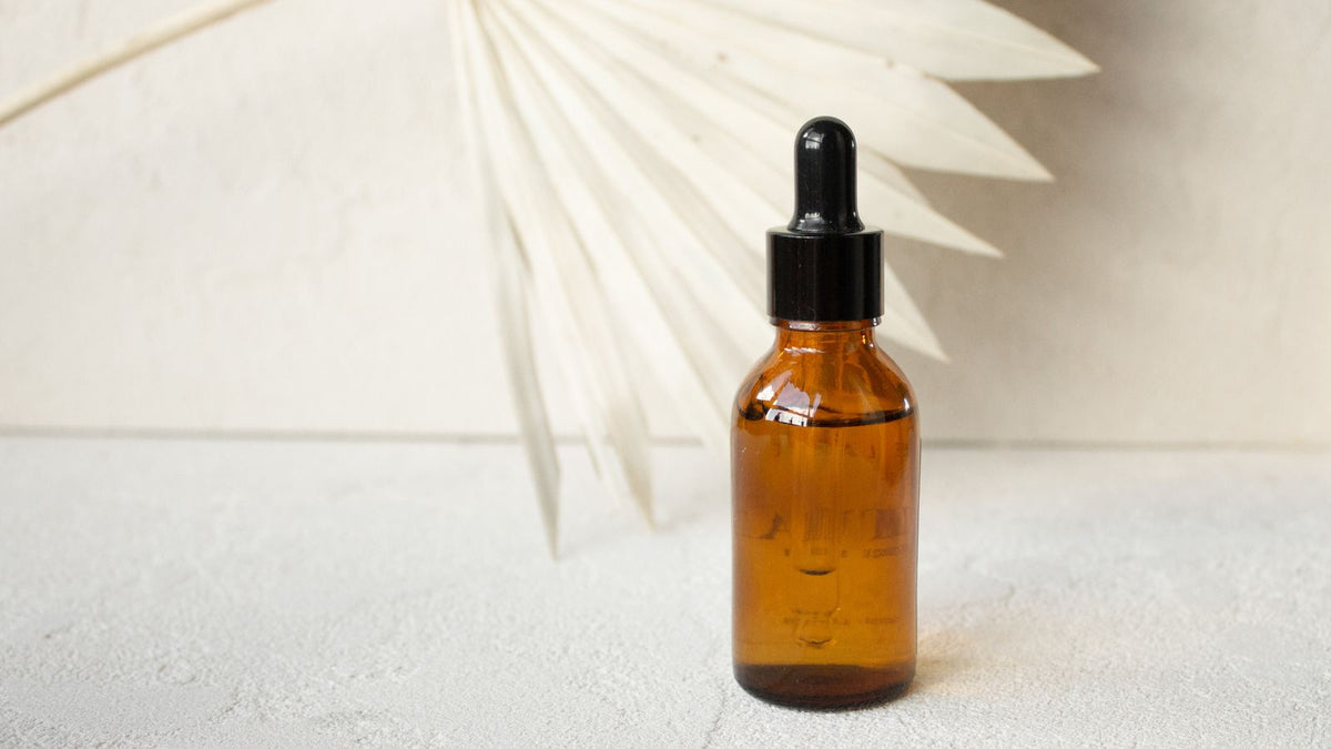 Amber glass dropper bottle of tamanu oil for hair on a neutral background