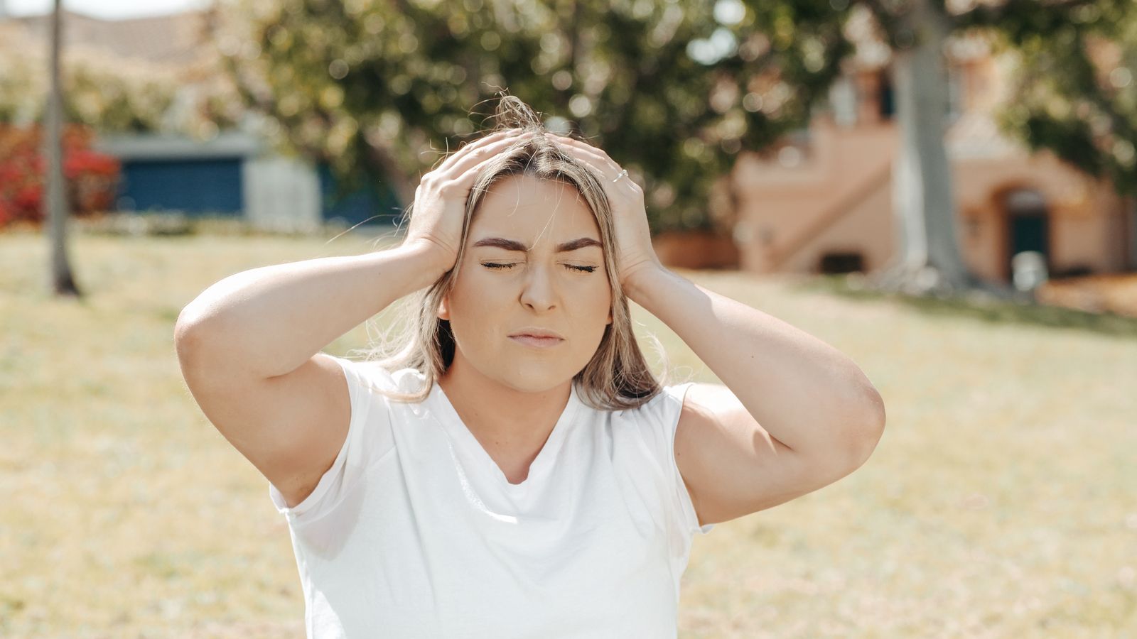 Woman holding her head outdoors, the ache of a tender scalp sits in the skin rather than the hair