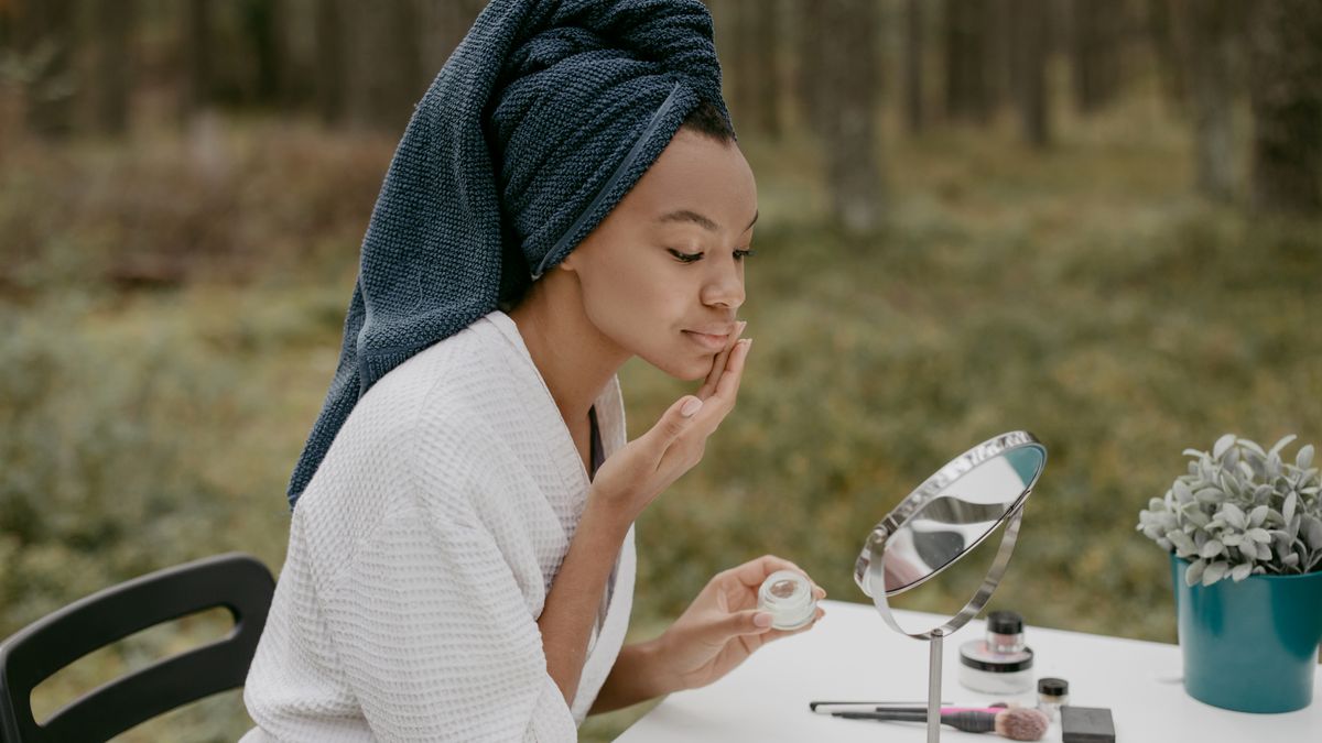 Woman applying facial cream in daylight, part of a daily routine against hyperpigmentation with tinted sunscreen