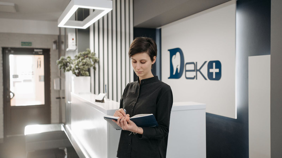 A receptionist taking notes at a clinic desk, the first stop when booking a trichologist Bexley appointment