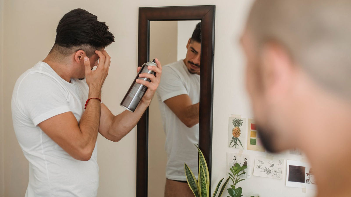 Man spraying hairspray onto his hair in front of a mirror, a daily styling habit people often ask a trichologist in Chester about