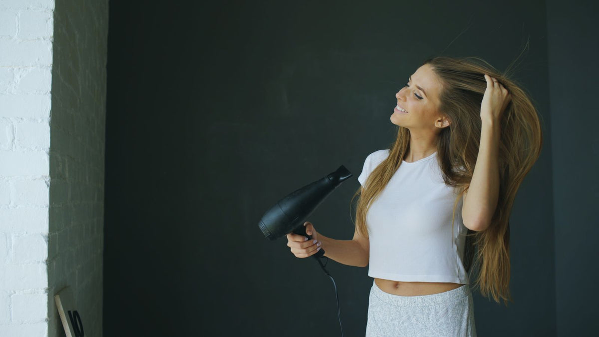 Woman blow-drying her long hair at home on a gentle setting, a routine worth checking before you look for a trichologist in Grimsby