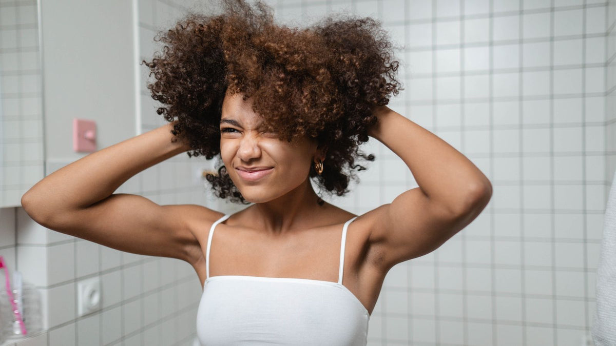 Smiling woman with natural afro hair on wash day in her bathroom, caring for coily hair before seeing a trichologist in Hastings