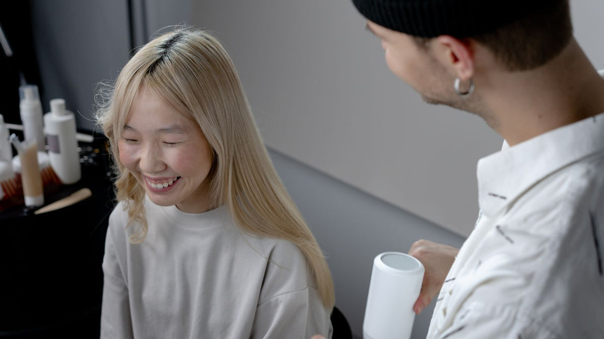Hairstylist blow-drying a smiling client's hair smooth in a salon, the kind of keratin blow-dry a trichologist in Southend-on-Sea is often asked about