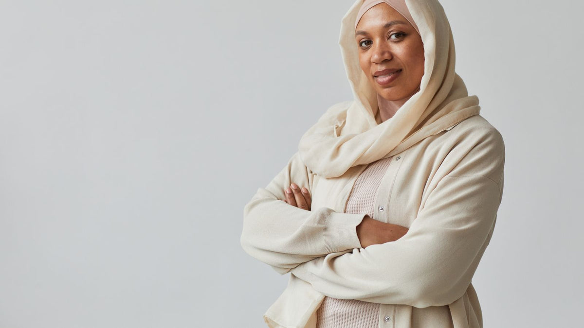 Woman wearing a cream hijab with her arms folded, the kind of daily head covering a trichologist in Stevenage should understand