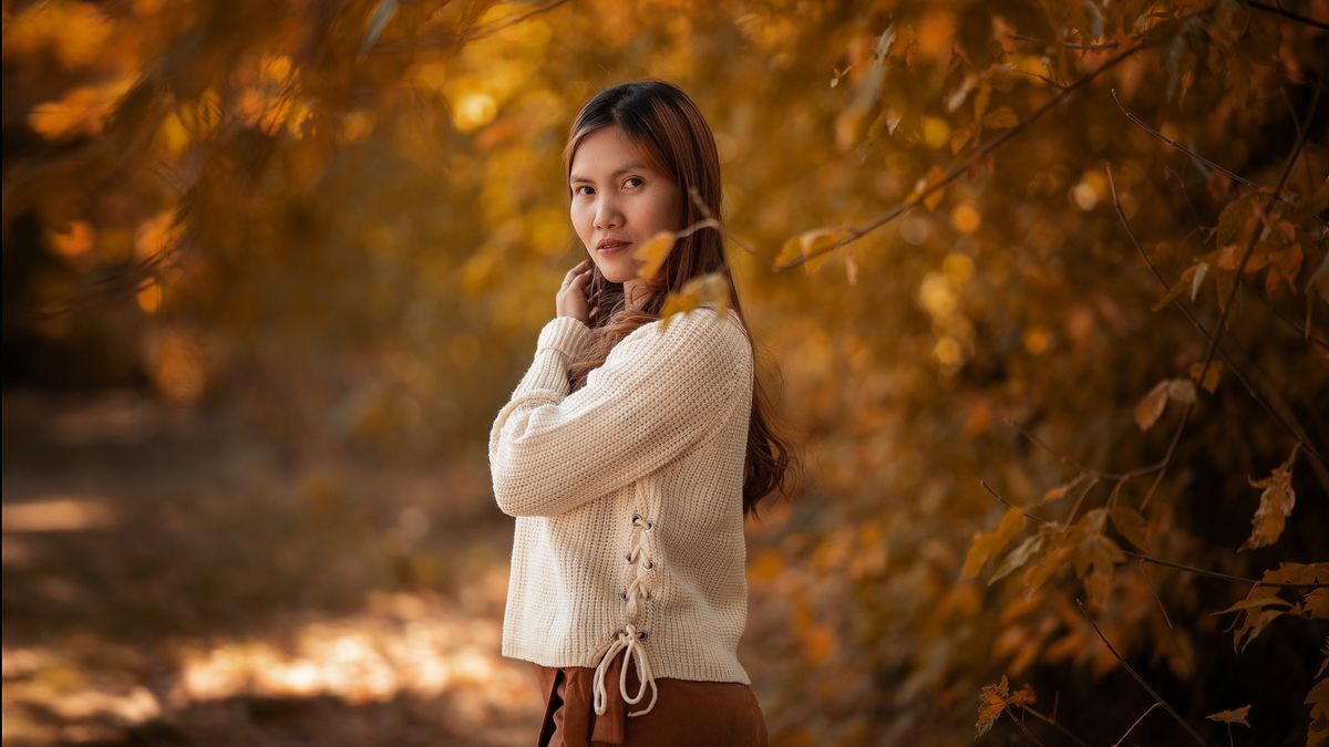 Woman with long hair among golden autumn leaves, the time of year many people start looking for a trichologist Reading can offer