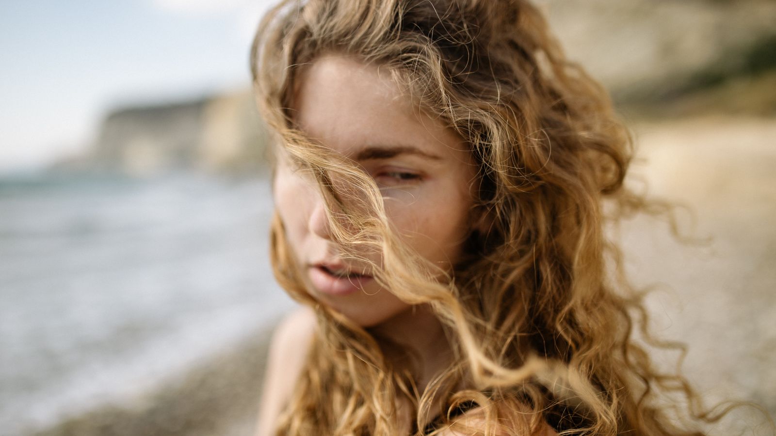 Woman with curly hair on a windy Devon beach, the sun and salt exposure a trichologist in Torquay sees