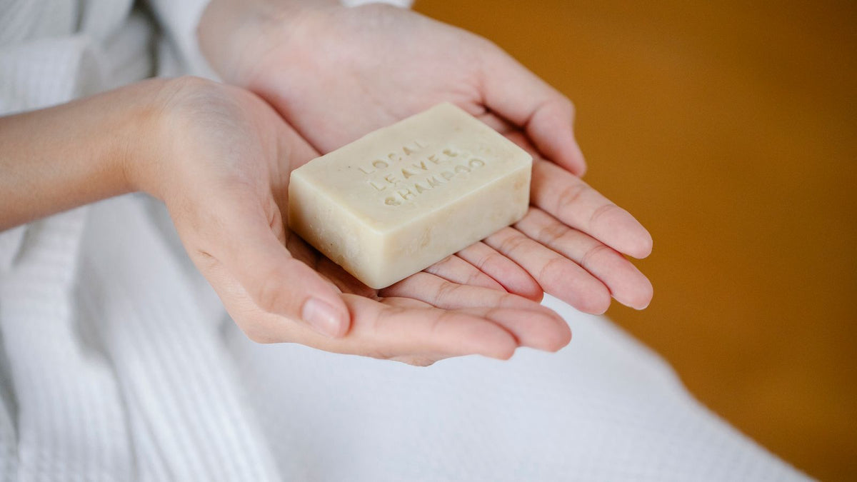 Hand holding a solid shampoo bar, weighed up against liquid shampoo for fine hair in a guide to trichologists Batley